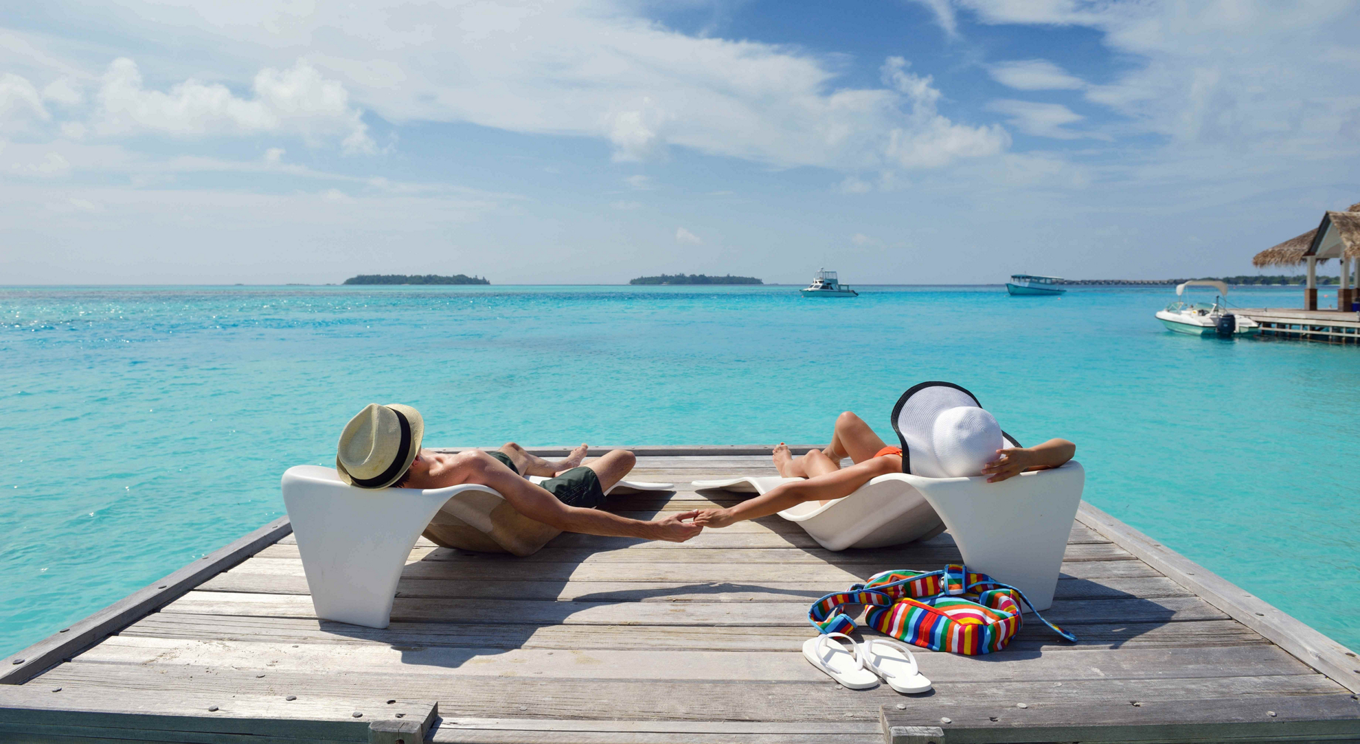 Best honeymoon destinations: A couple on sun loungers holding hands overlooking the ocean