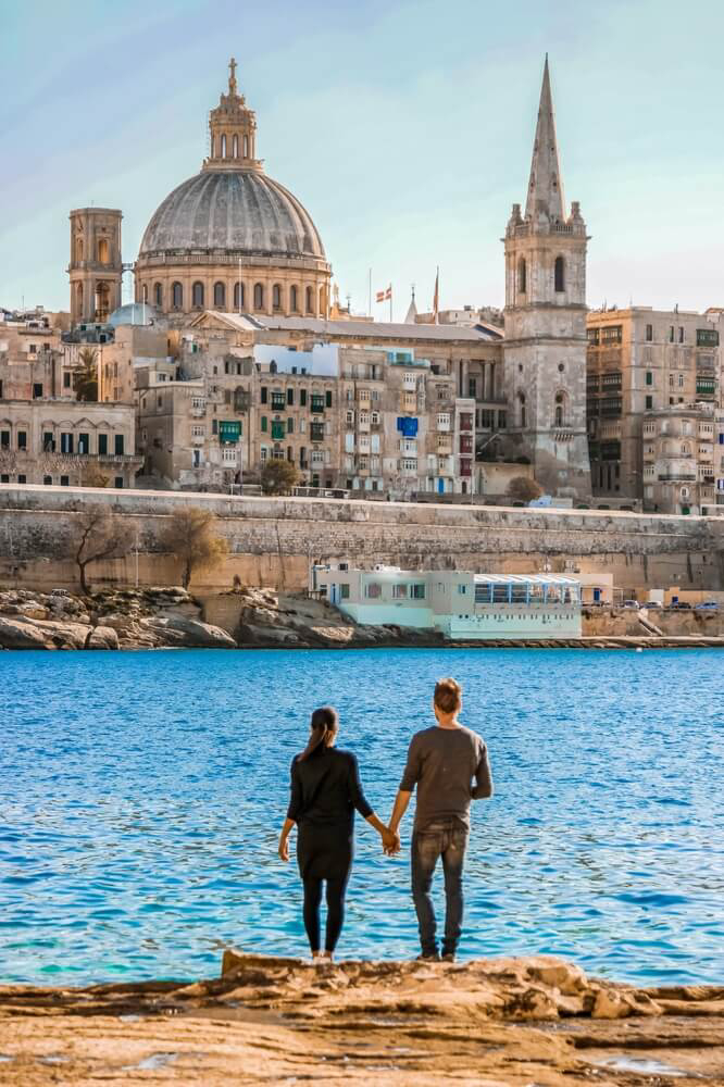 Malta: A couple standing on the water’s edge looking at an emblematic building