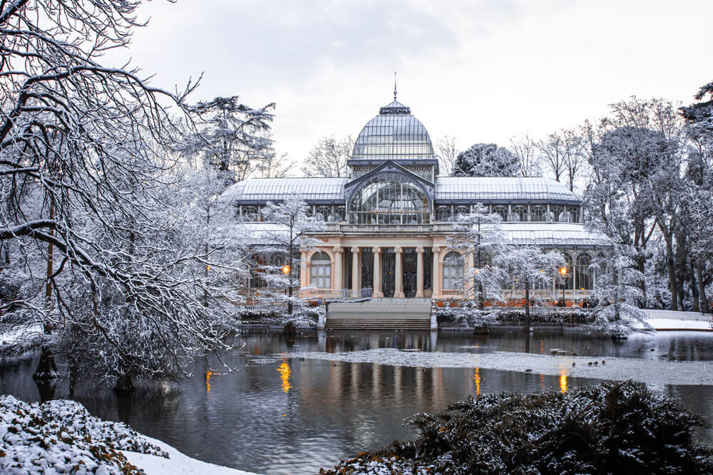 Best winter city breaks in Europe: Views across Retiro lake of the crystal palace covered in snow