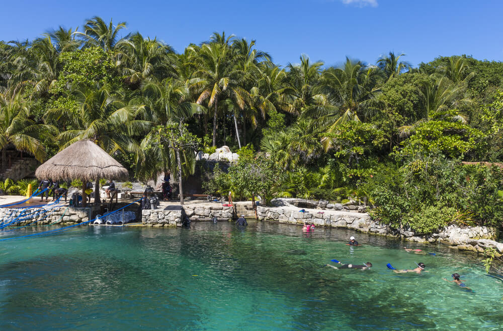 Black Friday travel deals: A cove with palms and people swimming at Xcaret Adventure Park, Mexico