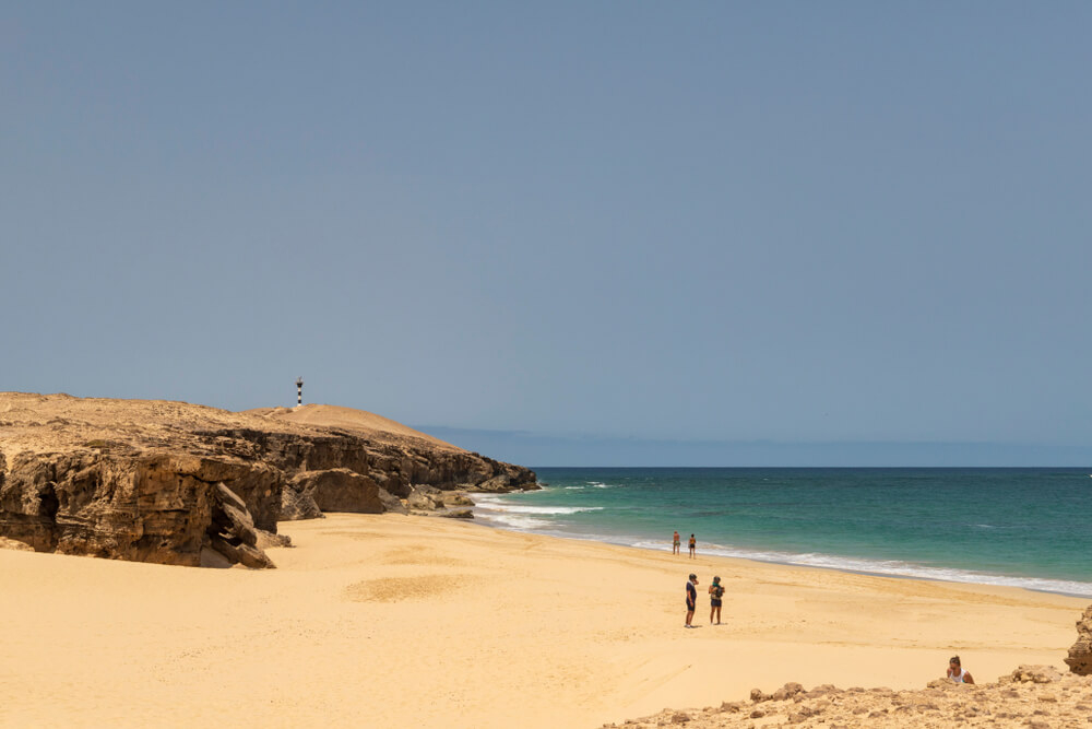 Boa Vista beaches: Golden sand beach sheltered by rocks with people and a lighthouse