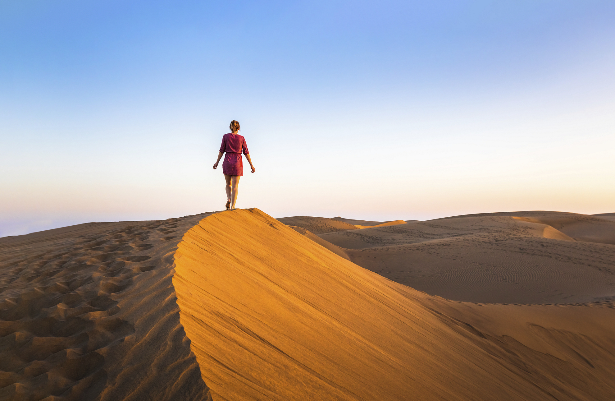 Girl walking on sand dunes in arid desert at sunset and wearing dress, scenic landscape of Sahara or Middle East
