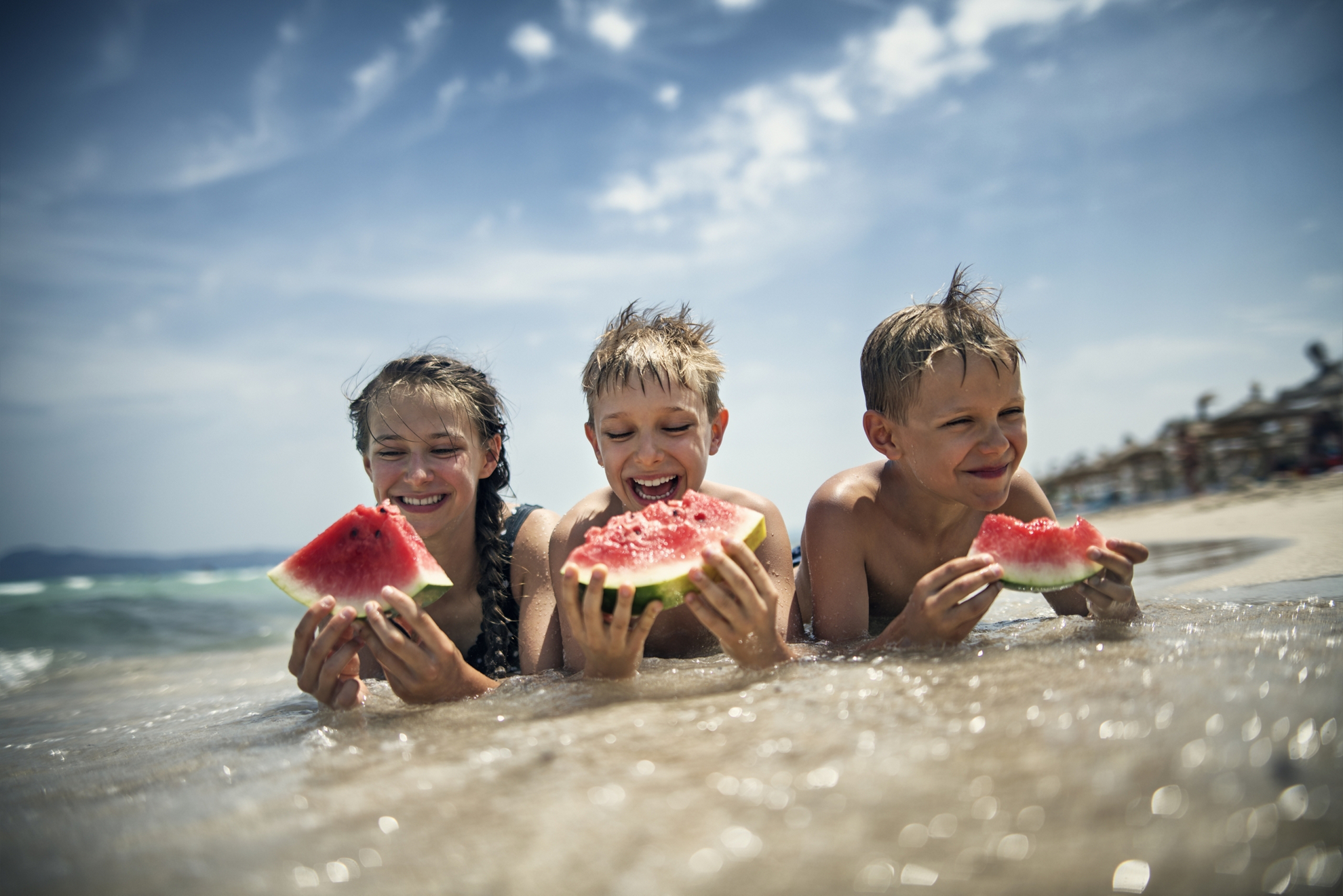 Brothers and sister eating watermelon on the beach on a sunny summer day.Nikon D850