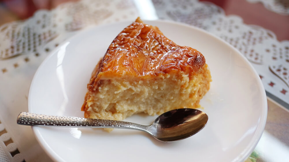 Quesillo Canario: A white plate with a golden cake and silver spoon on top