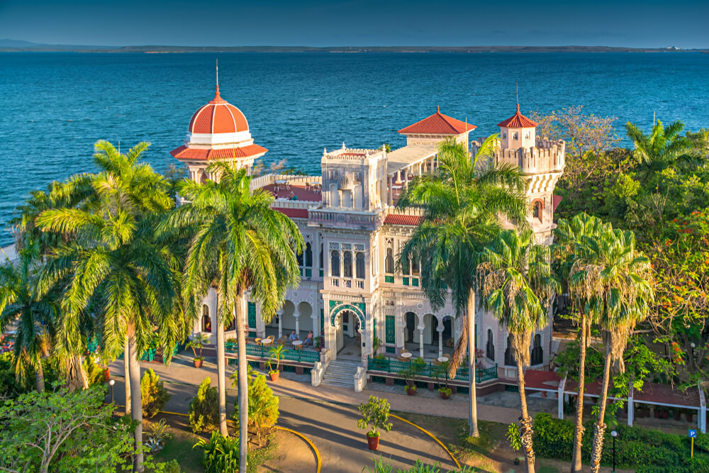 Cienfuegos: A ornate white large building surrounded the the sea and palms