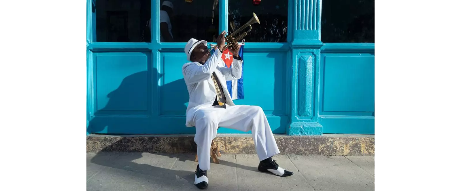 Cuban Culture: A man sitting on the sidewalk playing a trumpet