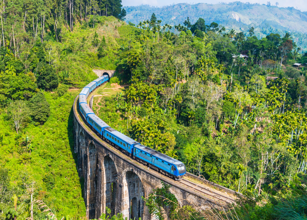 Blue train on the Nine Arches bridge, surrounded by trees near Ella, Sri Lanka