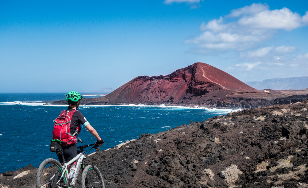 Cycling in Lanzarote: woman with bike on a mountain overlooking a volcano