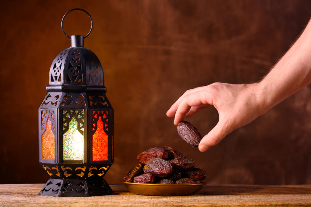 Eid al Fitr celebrations: A black lantern and a plate of dates with a hand holding one