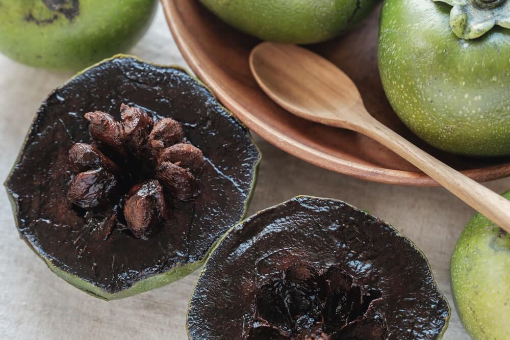 Black Sapote: A sliced open black sapote and entire green ones in a wooden bowl