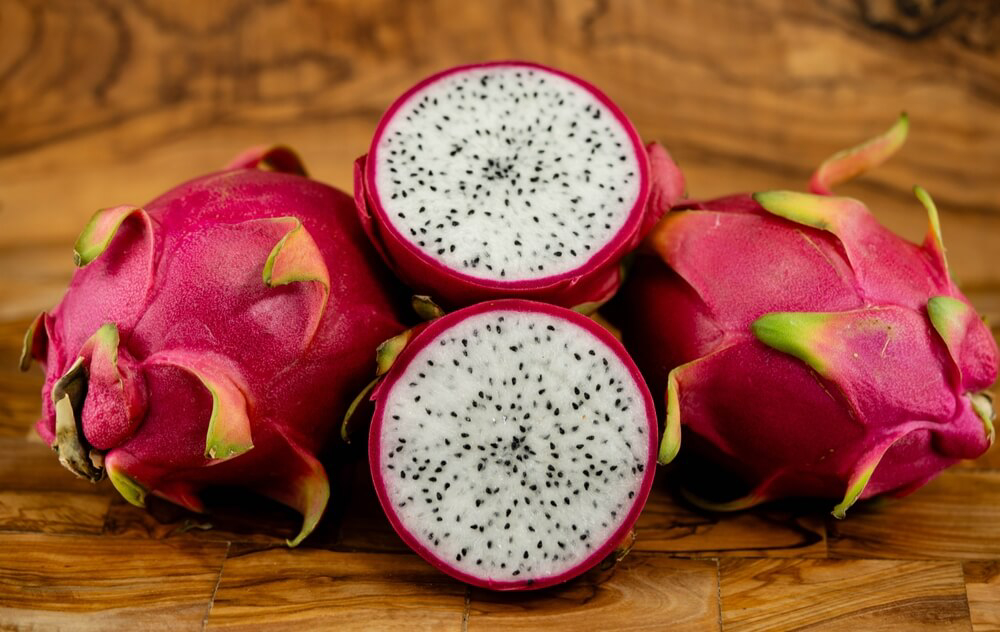 Dragon Fruit: Two entire dragon fruits and one sliced open on a wooden table