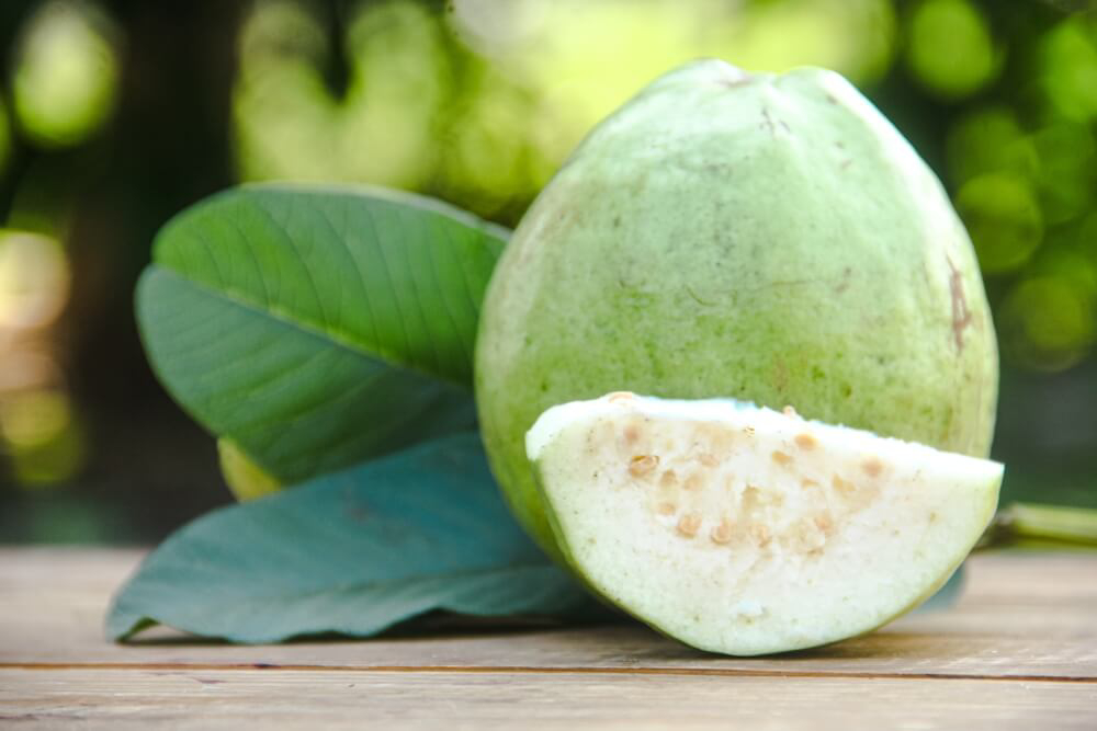 Guava: A wooden surface, outside, with a sliced open guava fruit on top