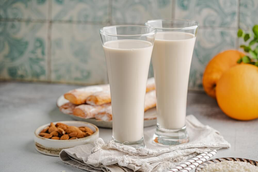 Two glasses of tiger nut milk, or horchata, sit in front of a plate of pastries