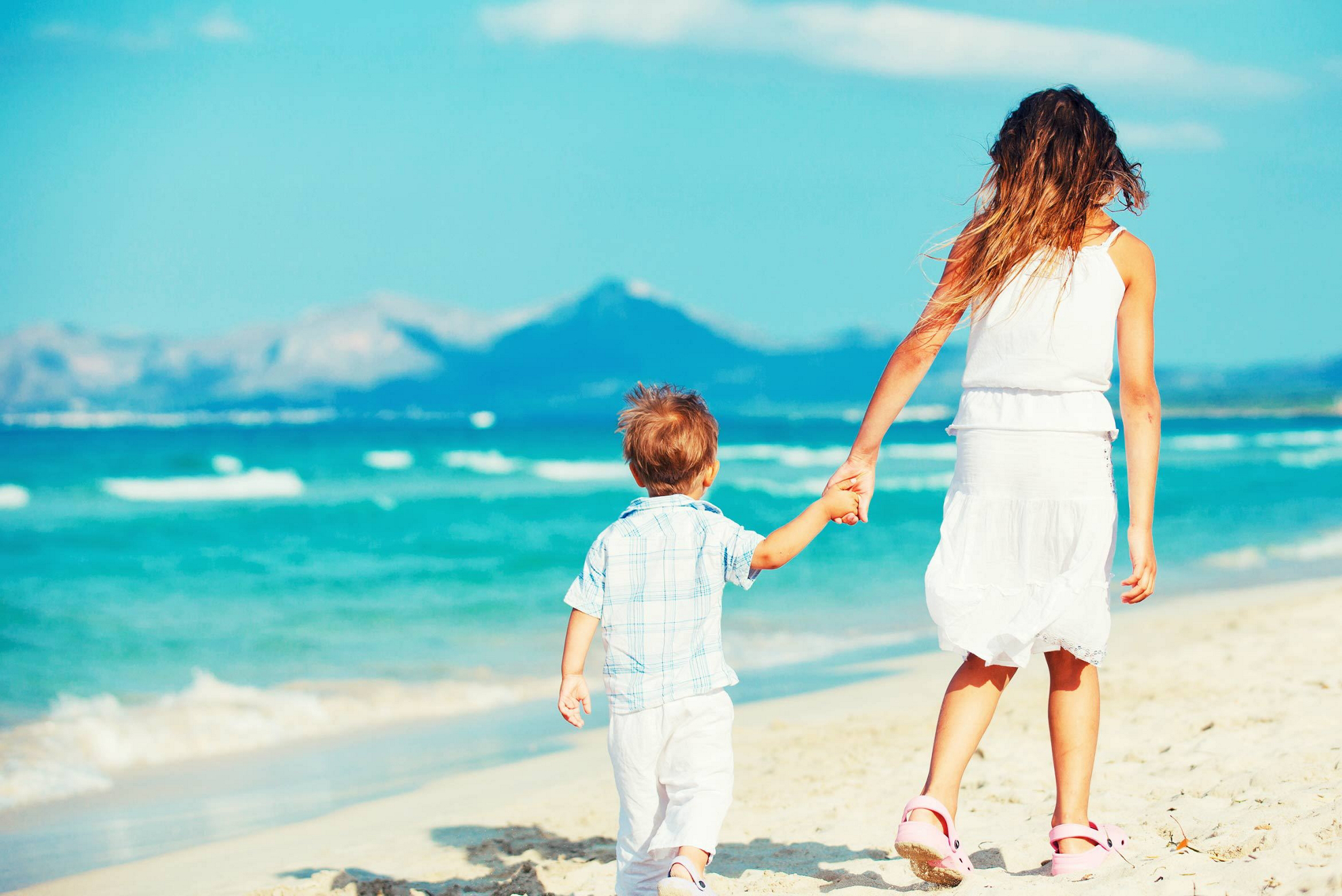 Family beach holidays: Two children walking along a white sand beach