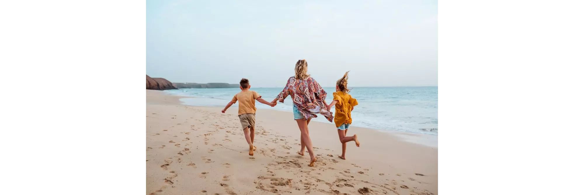 Family holidays in Lanzarote: A blonde haired woman walking hand in hand on the beach with two kids