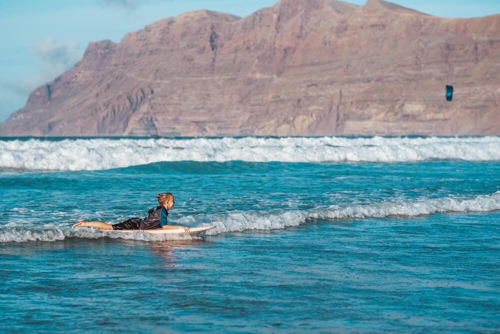 Water sports for kids in Lanzarote: A little girl surfing in the sea 