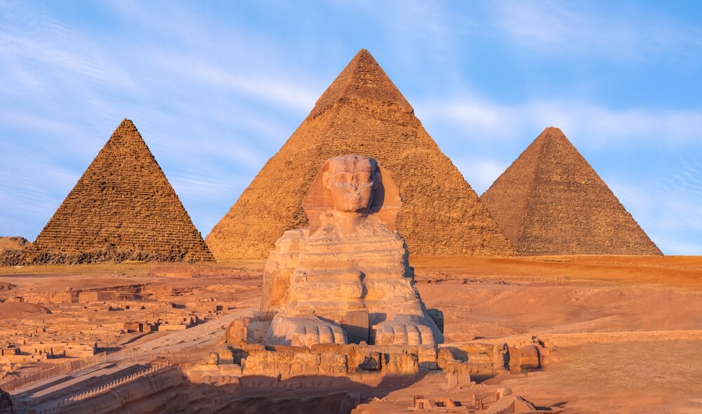 Pyramids: Three golden pyramids and the sphinx against the setting sun