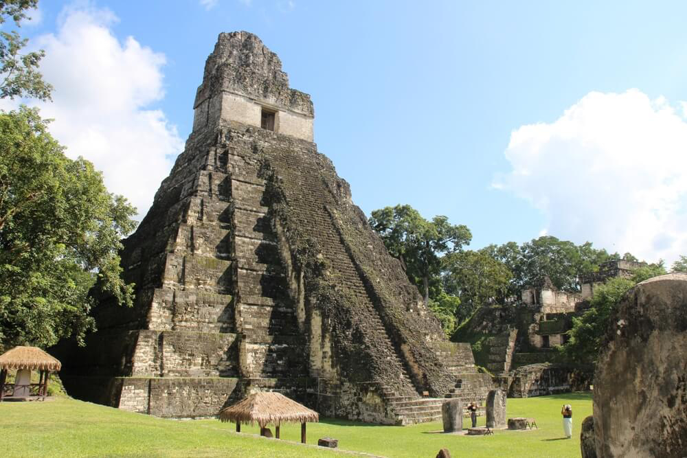 Tikal: A small but tall stone Mayan pyramid in a green field 