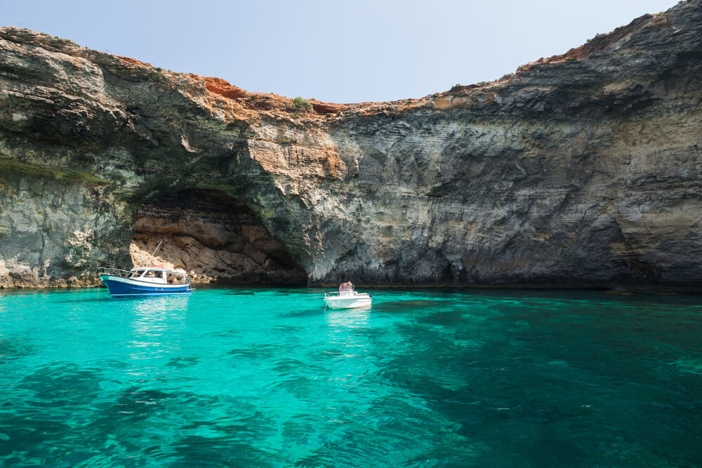 Ferien auf Malta: Boote in türkisblauer Lagune mit Felsklippen.
