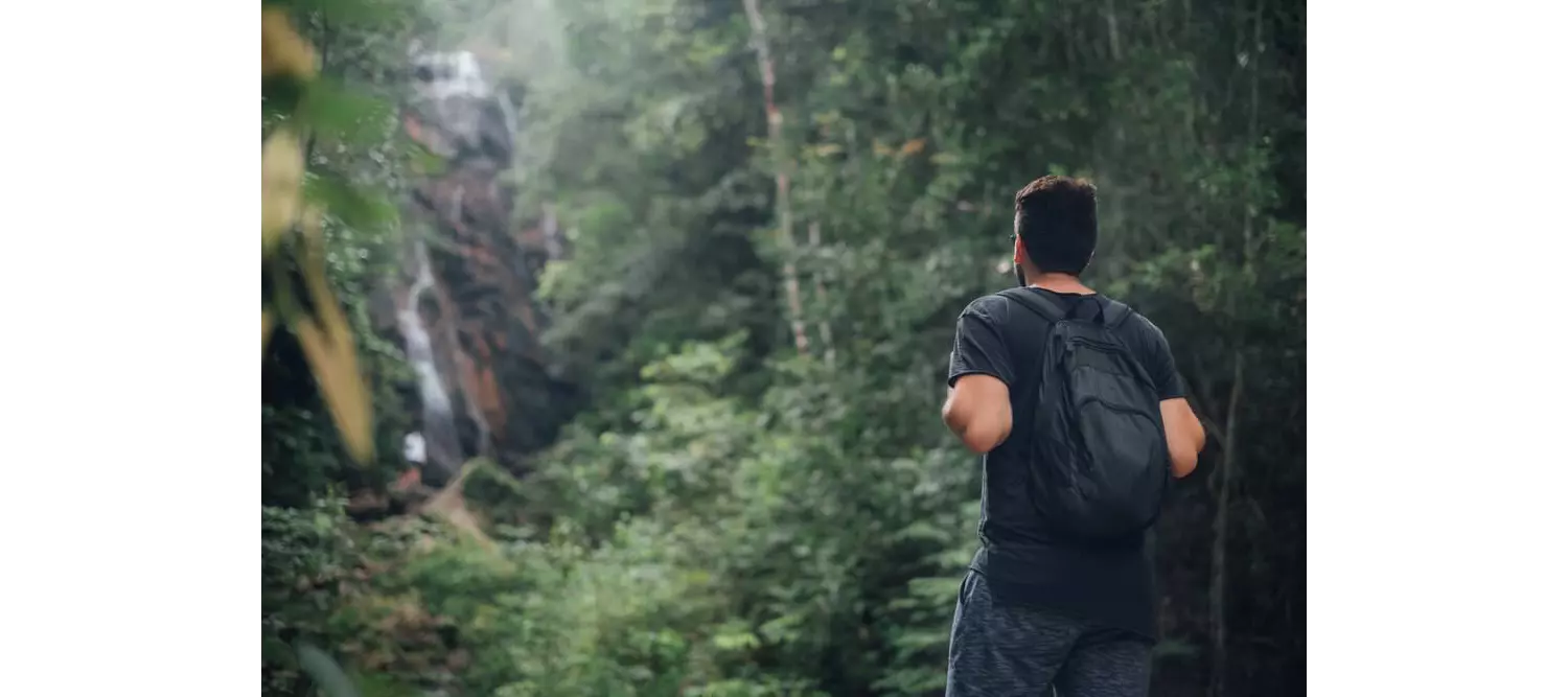 A man hiking in a tropical forest with a waterfall in the background. 