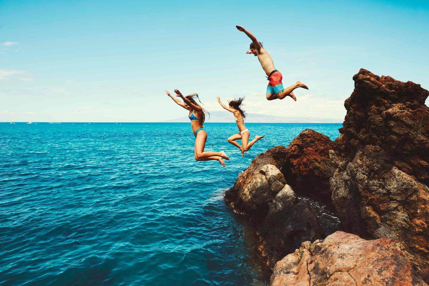 Group of friends jumping off cliffs into the sea