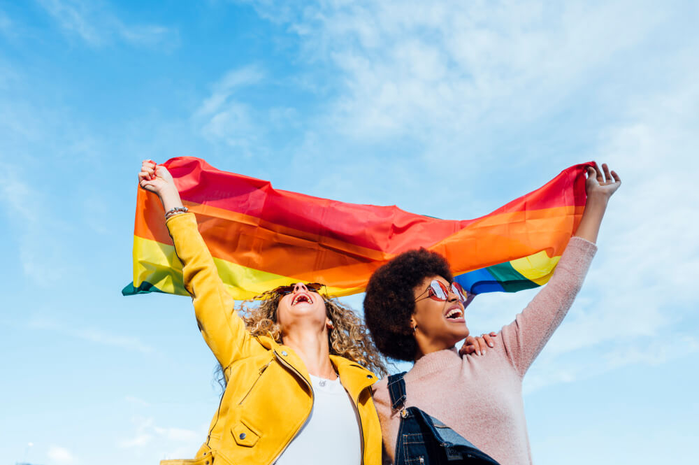 Two women hugging and waving the Pride rainbow flag