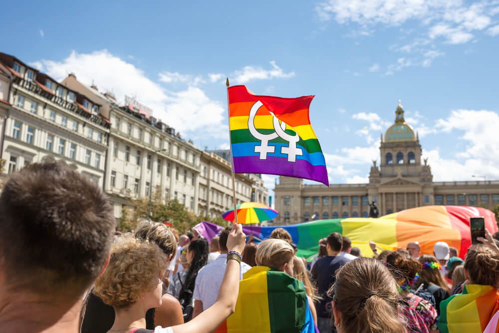 A crowd of people in the streets of Prague waving rainbow LGBT flags