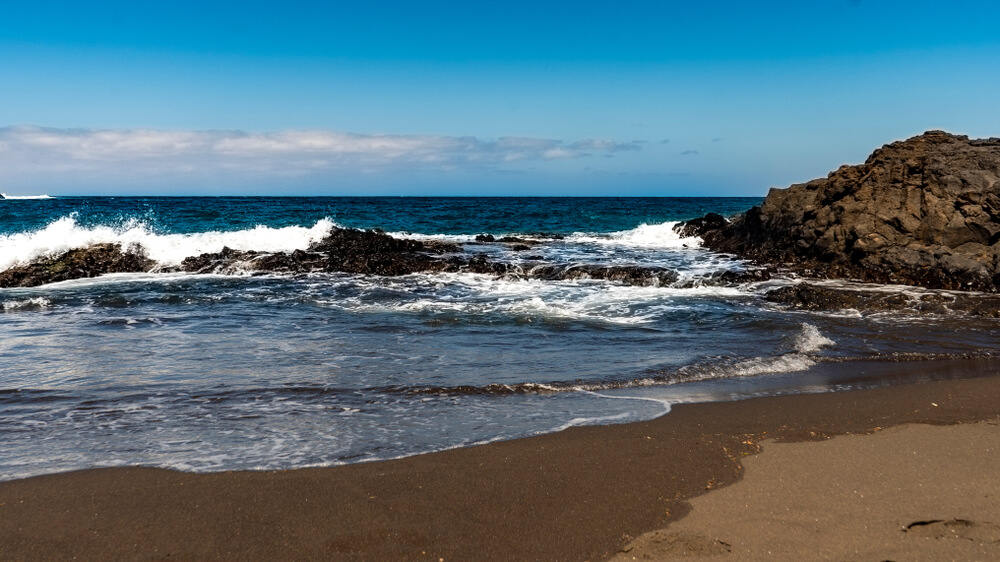 Schwarzer Sand und Felsen am Strand von Melenara auf Gran Canaria.