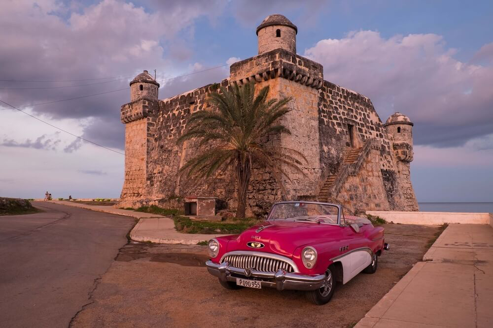 Cojímar: a close-up of a red car and an old tower at sunset