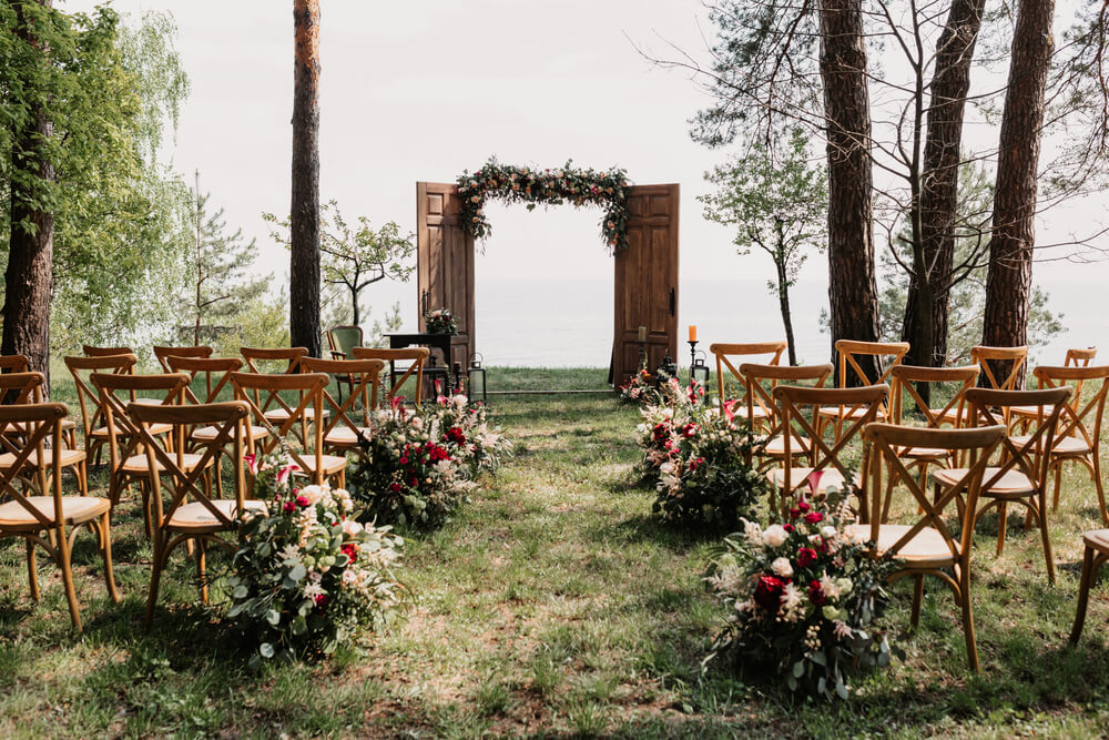 Hochzeit im Freien: Traualtar im Wald mit Stühlen und dem Meer im Hintergrund.