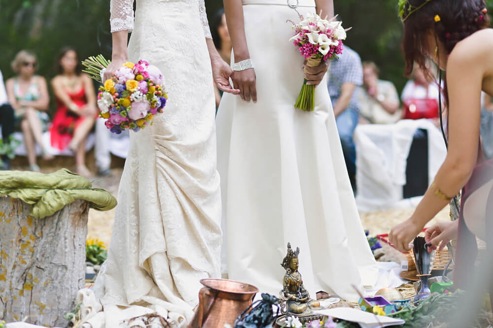 Hochzeit im Freien: weibliches Brautpaar im Wald mit Hochzeitsgesellschaft im Hintergrund