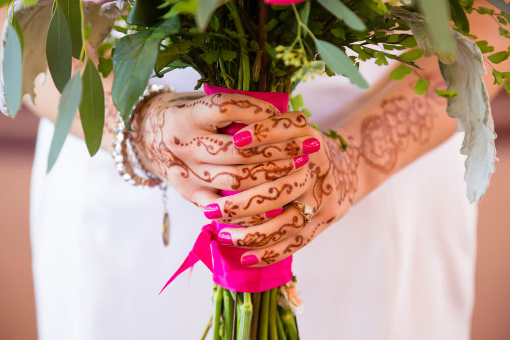 Hochzeitsrituale weltweit: Braut mit Henna-Verzierungen trägt einen Blumenstrauß in den Händen.