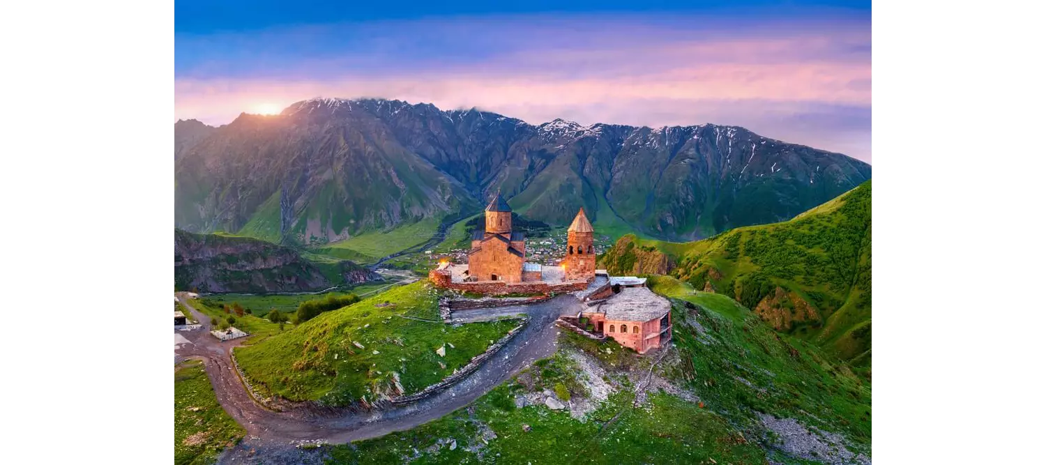 Kazbegi: A green mountainside with an old church building in the middle of nowhere