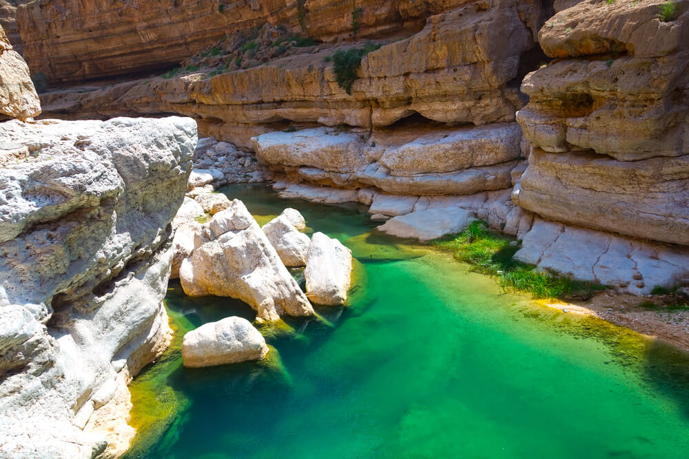 Famous sights in Oman: The green water and sandy cliffs of the Wadi Shab gorge