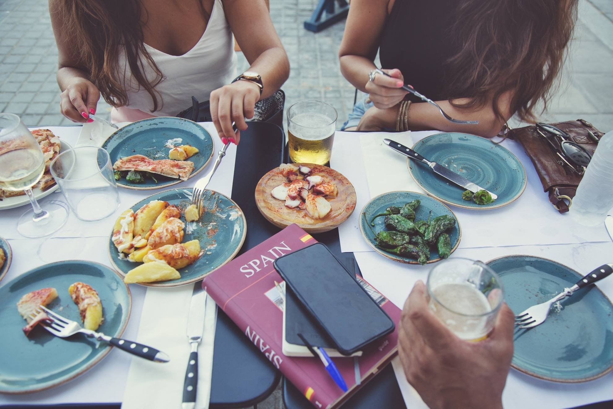 Tourists in Barcelona eating tapas in a typical restaurant in the Barri Gotic. On the table a travel guide of Spain and a smartphone.
