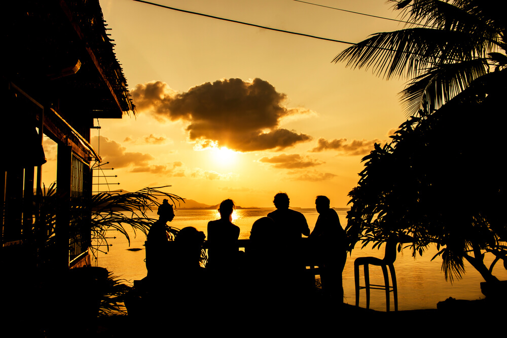Boat Party: A group of people sitting on the shoreline at sunset