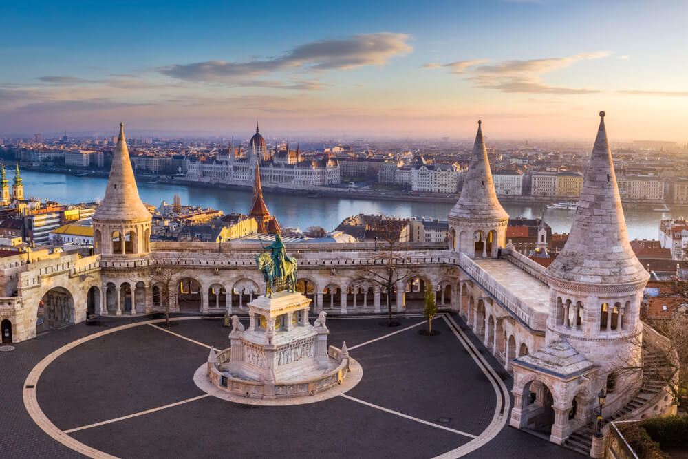 Fishermans Bastion Budapest: A white fortress with turrets against a river at sunrise