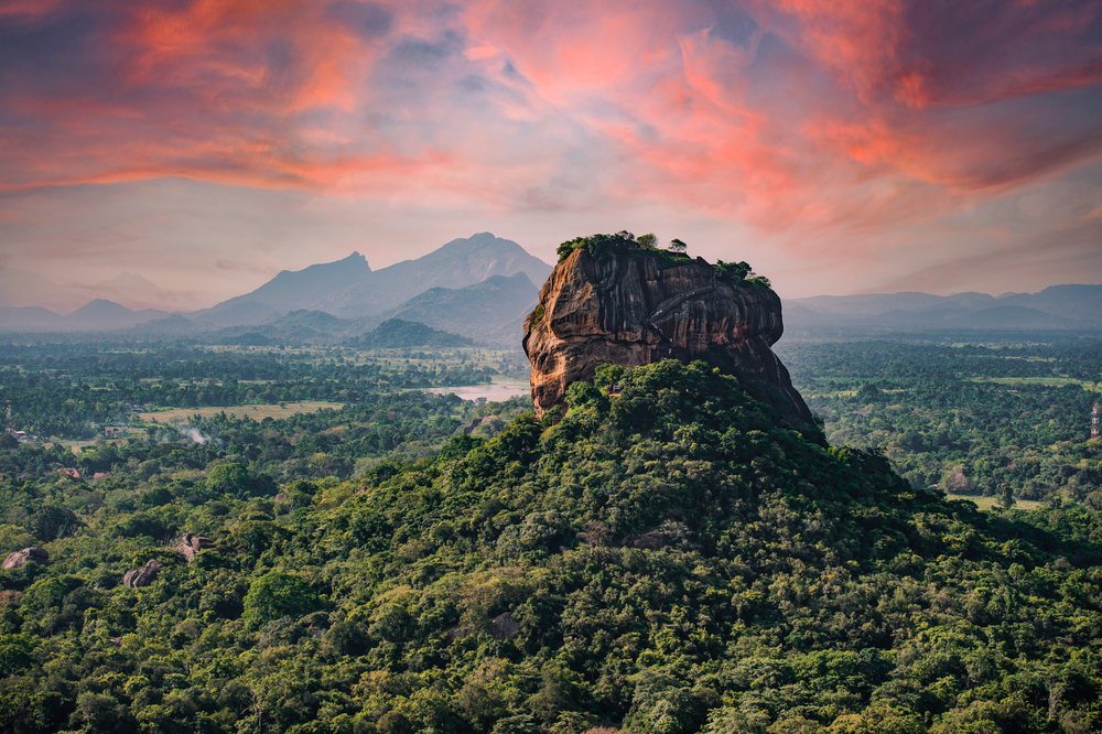 Sigiriya Rock: A mountain with a flat top surrounded by greenery at sunset