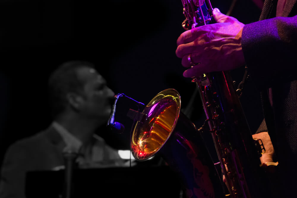 Saxofonist auf einer Bühne mit Pianist im Hintergrund.