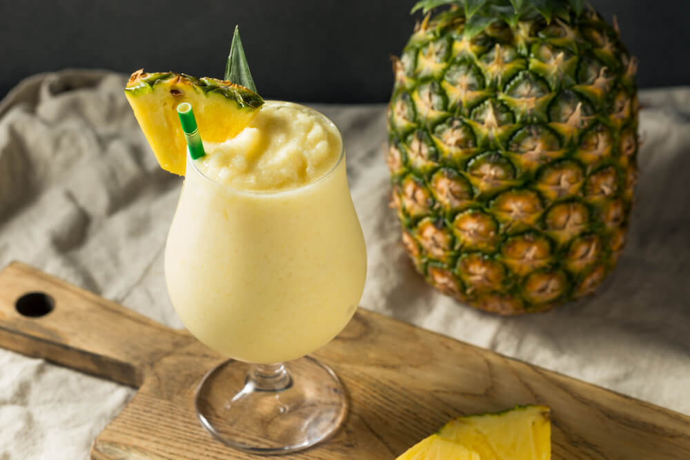 Karibische Cocktails: Glas mit hellgelbem Drink und Ananas daneben
