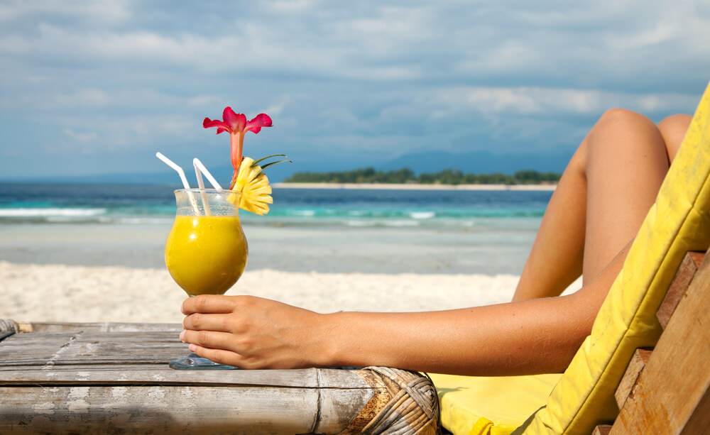 Karibische Cocktails: Frau mit Drink auf einem Liegestuhl am Strand