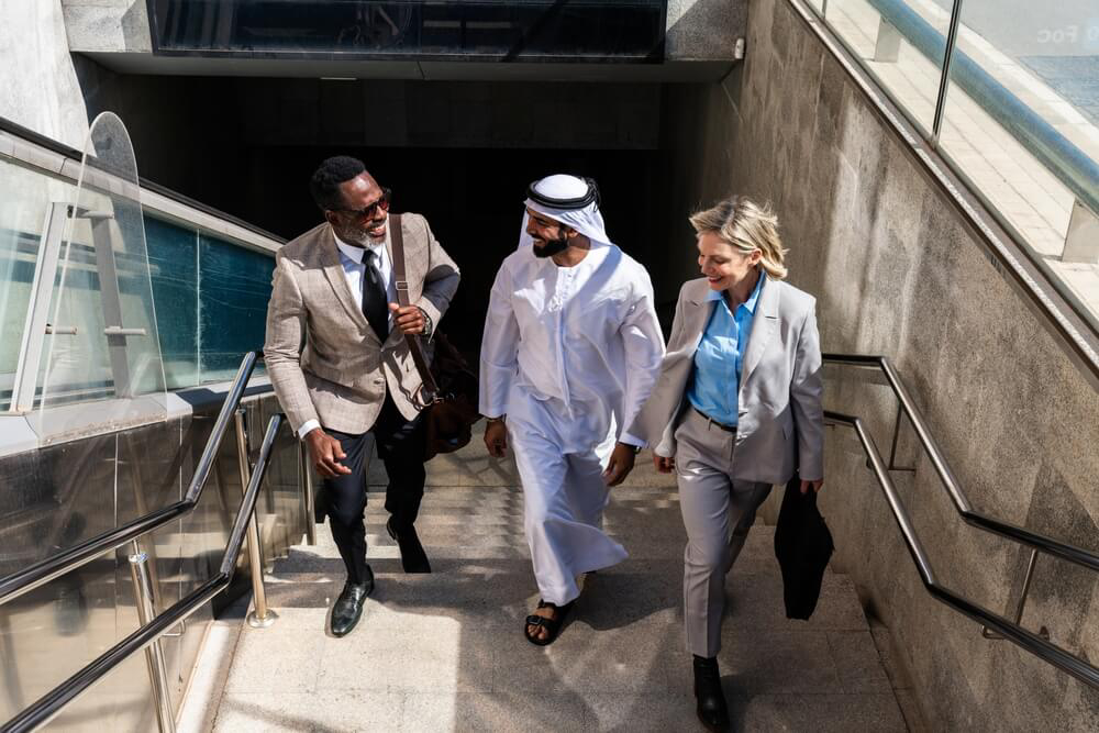 Kleidung in Dubai: Mann mit arabischer Kleidung neben Mann und Frau mit westlicher Kleidung.