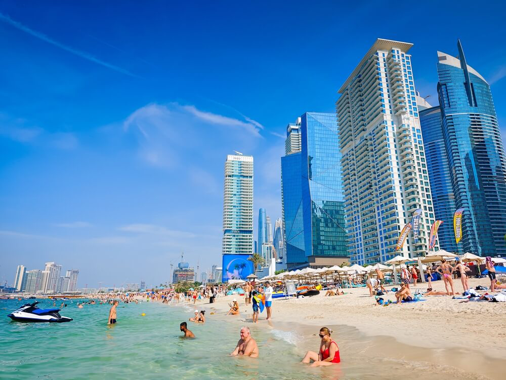 Strand voller Menschen vor hoher Gebäudekulisse in Dubai.