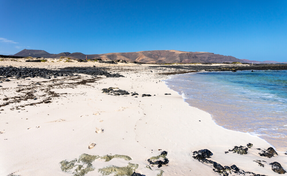 Weißer Sand und schwarzes Vulkangestein a der Caleta del Mero auf Lanzarote.