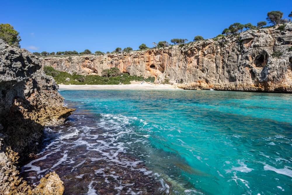 Türkisblaues Wasser, hohe Steilküste und weißer Sand an der Cala Magraner.