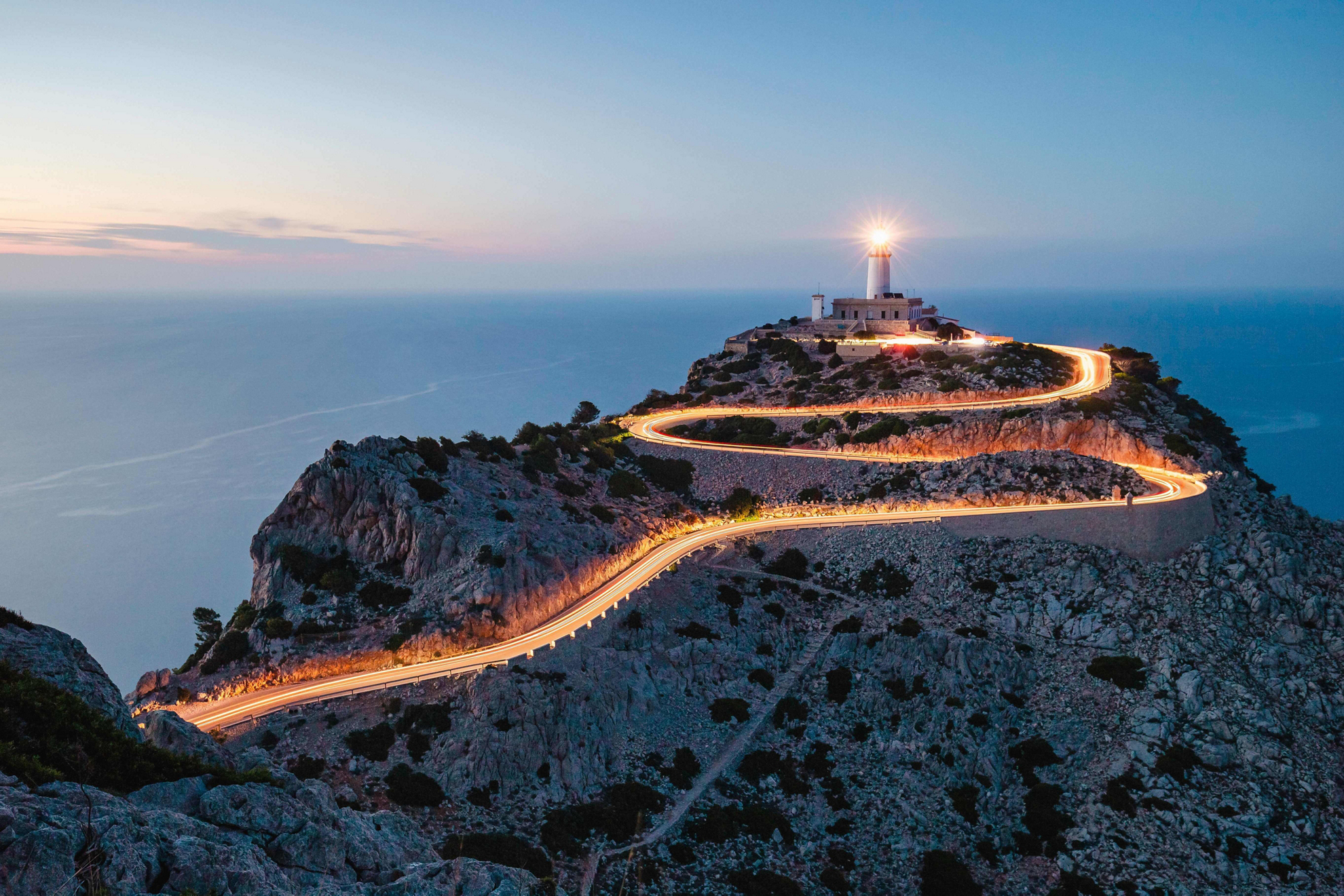 Mallorca for couples: A winding, lit-up mountain road with a lighthouse at the end