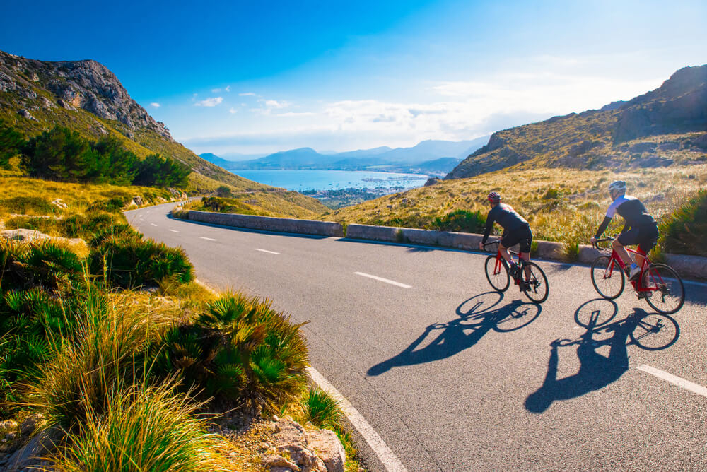 Landstraße auf Mallorca mit zwei Radfahrern und Aussicht aufs Meer