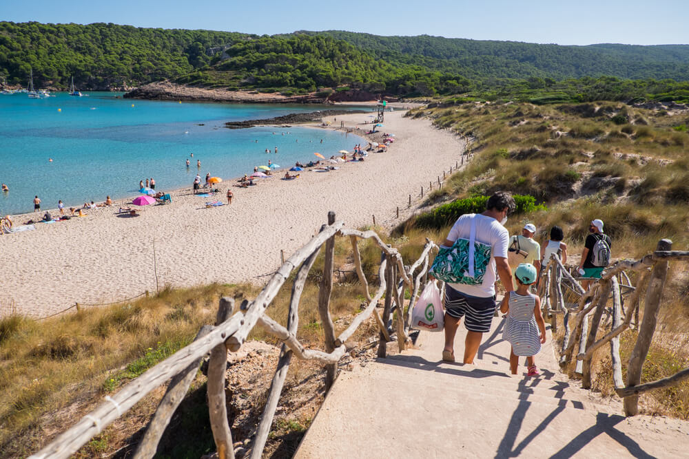 Eine Familie wandert in die naturbelassene Bucht Cala Algaiarens auf Menorca.