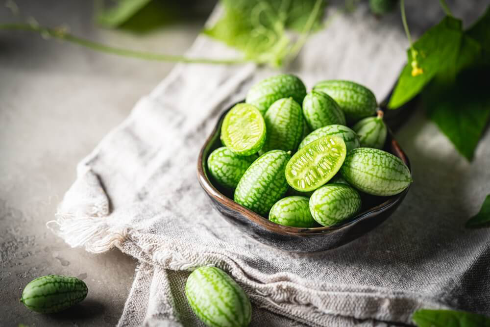 A bunch of cucamelon fruits in a tiny bowl on top of a folded cloth napkin.