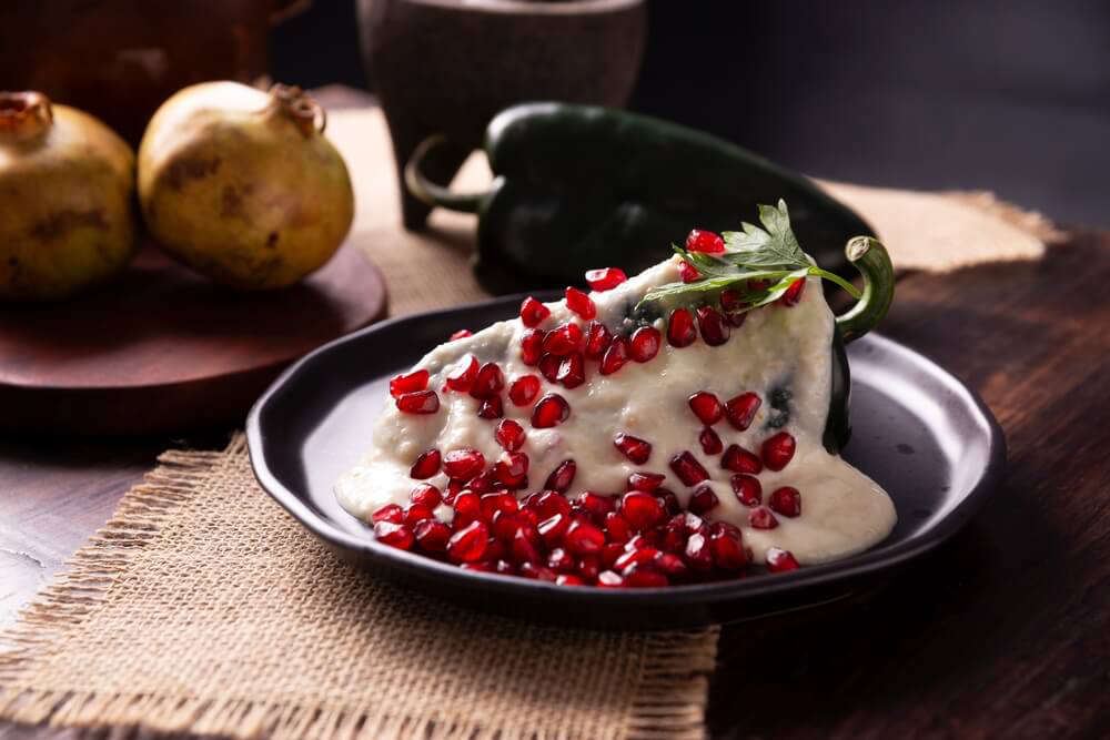 A dish of chiles en nogada, a green poblando pepper, white sauce, and pomegranate seeds.